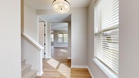 This two-story home is thoughtfully designed across two floors, with the main level housing the primary living spaces and the upper level dedicated largely to bedrooms and bathrooms. The main floor features an open-concept kitchen, dining room, and living room, all finished with light hardwood-style flooring that runs consistently throughout the home, contributing to a bright, cohesive aesthetic. The kitchen is a standout, equipped with rich dark-stained cabinetry, white quartz countertops, stainless steel appliances, a geometric tile backsplash, and a central island with a pendant light above. The dining area is bathed in natural light through large windows dressed with horizontal blinds, accompanied by an overhead pendant fixture. The upper floor hosts three bedrooms, each featuring neutral gray walls, light wood flooring, and generous windows that invite natural light. The primary bedroom offers comfortable proportions. Three bathrooms serve the home; one features a glass-enclosed walk-in shower with large-format gray tile, a built-in bench, and hexagonal mosaic tile flooring, while another includes a soaking tub with full tile surround. A dedicated laundry room with natural light completes the upper level.