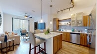 This well-designed single-floor residence offers a cohesive blend of modern aesthetics and functional living. The open-concept layout connects the kitchen and living area seamlessly, creating an inviting, airy atmosphere. The kitchen is a standout feature, showcasing warm wood-tone flat-front cabinetry, light blue subway tile backsplash, stainless steel appliances including a refrigerator, range, microwave, and dishwasher, and a central island with a white quartz countertop and bar seating. Pendant lighting and a rail track light system illuminate the space with precision. The living area flows naturally from the kitchen and is bathed in natural light from a large sliding glass door fitted with vertical blinds that open to an outdoor balcony view. A ceiling fan adds comfort to the room. The bedroom is a calm retreat with light hardwood flooring, a ceiling fan, a large window with blinds for privacy, and a spacious walk-in closet. The full bathroom features clean white tile flooring, a wood-tone vanity with a white countertop, and a tub-shower combination. Completing the unit is a dedicated in-unit laundry area with a full-size washer and dryer. Throughout, light hardwood flooring and crisp white walls create a bright, modern ambiance.