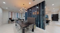 Located at 5005 Galleria Dr in Farmers Branch, TX, this single-floor amenity space delivers a polished, contemporary environment designed for both socializing and relaxation. The open layout is unified by large-format white tile flooring and recessed lighting that keeps the space bright and welcoming throughout.

A striking feature wall clad in deep blue and bronze streaked paneling serves as a dramatic focal point, anchoring both the lounge seating area and the adjacent dining zone. The dining area centers on a dark wood table paired with clear acrylic chairs and a multi-armed metallic chandelier overhead, while bold geometric artwork adds visual energy to the walls.

The wet bar area is sleekly outfitted with matte black cabinetry, a teal glazed subway tile backsplash, a glass-top angular island with built-in wine storage, globe pendant lights, and stainless steel appliances including a beverage refrigerator. A wall-mounted television and sink make this a fully functional entertaining hub.

Floor-to-ceiling glass walls along one side of the space invite abundant natural light and provide open views to the exterior. The lounge area offers comfortable seating around a television mounted on the signature feature wall, while the game room includes a shuffleboard table. Together, these zones create a cohesive, upscale communal retreat.