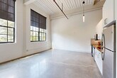 Unit 102 at 3511 Tire Towne Rd is a thoughtfully designed 2-bedroom, 2-bathroom residence that blends industrial character with contemporary finishes. The open-plan kitchen and living area serves as the heart of the unit, showcasing soaring ceilings with exposed beams and ductwork, gleaming polished concrete floors, and oversized factory-style windows with roller shades that flood the space with natural light and offer views of mature trees outside. The kitchen features white cabinetry, a butcher block countertop, stainless steel appliances, and a subway tile backsplash. Both bedrooms continue the polished concrete flooring aesthetic, with the primary bedroom benefiting from impressive ceiling height and an open, airy feel. The unit includes three closets and a dedicated laundry space for added convenience. The bathrooms are finished to a high standard: one features a soaking tub with floor-to-ceiling white tile surround, while the other offers a sleek, wall-mounted double vanity with dark cabinetry, brushed nickel fixtures, backlit mirrors, and terrazzo-style concrete flooring. A connecting hallway ties the layout together efficiently. This unit's adaptive-reuse industrial aesthetic makes it a distinctive and functional living space in Winston-Salem.