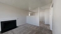 Located at 8812 Avril Ct S in Fort Worth, TX, this single-floor unit offers a well-organized layout comprising a living room, kitchen, bathroom, and closet. The living room serves as the central gathering space, highlighted by a wood-burning fireplace with a clean white mantel and black surround. Soft, neutral-toned carpet extends throughout, complemented by light gray walls and a textured popcorn ceiling. A large window floods the room with natural light, enhancing the open, airy feel. A half-wall partition defines the space while maintaining visual connectivity to the rest of the unit. The kitchen is fitted with white cabinetry above and below the counter, a speckled laminate countertop, a double stainless steel sink, a range hood, and a black dishwasher. Tile flooring grounds the kitchen area practically. The bathroom includes a full-size soaking tub and shower combination, a toilet, and built-in shelving, finished with tile flooring. A dedicated closet provides additional storage. Throughout the unit, the neutral color palette and clean finishes create a cohesive, functional living environment suited for everyday comfort.