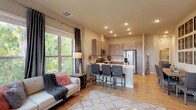 This single-floor residence offers a thoughtfully designed open-concept layout that seamlessly connects the living area and kitchen. The living room is bathed in natural light through large windows dressed with elegant floor-to-ceiling curtains, offering pleasant outdoor tree views. Light hardwood flooring flows throughout the main living areas, adding warmth to the neutral color palette.

The kitchen is outfitted with taupe shaker-style cabinetry, stainless steel appliances including a refrigerator with water dispenser, electric range, and over-the-range microwave, all complemented by clean white countertops. A peninsula with bar seating provides a casual dining option and enhances the open feel of the space.

The primary bedroom features plush carpeting, a ceiling fan, and a window with outdoor views, while a second bedroom is equally comfortable with generous natural light. Both bathrooms are well-equipped — one features a tub/shower combo and access to a walk-in closet, while the other includes an extended vanity with ample cabinetry and a linen tower for additional storage. Recessed lighting throughout the home ensures a bright and welcoming ambiance across every room.