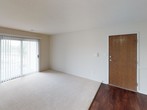 This 2-bedroom, 1.5-bathroom single-floor residence offers a functional and well-organized layout designed for comfortable everyday living. The entry opens into a spacious living area featuring rich dark hardwood flooring that transitions into plush carpeting, a ceiling fan, and a sliding glass door with vertical blinds that invites natural light and provides outdoor access. The galley-style kitchen is efficiently designed with warm wood cabinetry, dark granite-style countertops, a double stainless steel sink, and black appliances including a refrigerator, electric range, and built-in microwave, all set over hardwood flooring. Both bedrooms are carpeted and offer bright, neutral walls with ample room for furnishings. The primary bedroom connects to a full bathroom and features access to a closet, creating a private and convenient retreat. The full bathroom includes a combined tub and shower with chrome fixtures, while the half bathroom features a warm wood vanity with a white countertop, an integrated sink, and a well-lit mirror with a multi-bulb vanity fixture above. Throughout, the unit maintains a clean, neutral palette with white panel doors and light-toned walls that lend a fresh, move-in-ready feel.