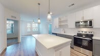 Located at 1290 Old Peachtree Rd NW in Duluth, GA, this single-floor residence offers a clean, contemporary design with thoughtfully selected finishes. The open-concept kitchen serves as the heart of the space, showcasing a generous central island with a crisp white quartz countertop, two-tone cabinetry in white and slate gray, a classic subway tile backsplash, and a full suite of stainless steel appliances including a refrigerator with ice maker, range, and microwave. Pendant lighting adds a modern touch above the island. Light wood-look flooring flows throughout the main living and kitchen areas, creating a warm and cohesive aesthetic. The living area benefits from natural light streaming through multiple windows dressed with blinds, offering views of the surrounding community. The bedrooms feature plush carpeting and ceiling fans, with windows that further enhance the bright, airy feel. The bathrooms are finished with gray vanity cabinetry, white countertops, subway-tiled tub-shower combinations, and brushed nickel fixtures, maintaining the unit's consistent modern style. A walk-in closet is accessible from the primary bathroom. The overall design emphasizes clean lines, neutral tones, and functional layouts, making this a well-appointed and move-in-ready residence.