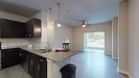 Located at 8003 IH-35 N in Austin, Texas, this single-floor residential unit offers a well-designed layout with contemporary finishes throughout. The kitchen is a standout feature, equipped with dark espresso cabinetry, granite countertops, a classic white subway tile backsplash, and a full suite of stainless steel appliances including a range, over-the-range microwave, and French door refrigerator. A peninsula with pendant lighting above serves as both a workspace and casual dining area, opening directly into the living space. The living area is bright and welcoming, with wood-style flooring, a ceiling fan, and a sliding glass door that invites natural light and provides access to an outdoor view. The bedroom is generously sized, featuring a ceiling fan, a large window overlooking greenery, and wood-style flooring. Double doors open into a walk-in closet outfitted with built-in shelving and hanging rods, offering ample organized storage. The bathroom features a tiled shower-tub combination, dark cabinetry with granite countertops, and light wood-style flooring that ties the space together cohesively. Neutral wall tones and consistent flooring throughout create a unified and modern aesthetic.