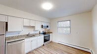 Located at 100 Norton Park Rd in Plainville, Connecticut, this single-floor residence offers three bedrooms and one bathroom across a compact, efficiently laid-out floor plan. The kitchen is well-appointed with white shaker-style cabinetry, granite countertops, a subway tile backsplash, and a full suite of stainless steel appliances including a refrigerator, electric range, microwave, and dishwasher. Light wood-look flooring runs throughout the kitchen and main living area, complementing the bright, neutral color palette. The living area receives natural light through windows fitted with blinds and includes baseboard heating. The three bedrooms feature plush carpeting, closet storage, and baseboard heating, with the spacious primary bedroom offering generous room for furnishings. One bedroom provides convenient access to an in-unit washer. The bathroom is finished with large-format marble-style tile on both the floors and tub surround, paired with a classic white soaking tub and modern fixtures. Throughout the residence, a clean, updated aesthetic and practical amenities create a comfortable and functional living environment.