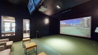 Located at 1412 E Mockingbird Ln in Midland, TX, this single-floor recreational facility is designed with a cohesive, modern aesthetic defined by dark walls, dramatic lighting, and high-end finishes throughout. The space is organized into several distinct zones, each purpose-built for entertainment and productivity.

The indoor golf simulator room is a standout feature, outfitted with artificial turf flooring, a large projection screen displaying full golf course simulations, an overhead projector, and an additional wall-mounted display. Warm wall sconces and built-in overhead lighting create a focused atmosphere ideal for practice or play.

Adjacent to the simulator is a billiards and social area centered around a solid wood pool table with a blue felt surface. A linear gas fireplace set into a wood-paneled accent wall, a wall-mounted television, and sleek linear ceiling lights lend the room a sophisticated, lounge-like character. Large interior windows connect this space visually to the rest of the facility.

A dedicated lounge area features rows of plush upholstered armchairs arranged for viewing or socializing, backed by a richly textured dark wood accent wall and a long credenza. Nearby, a smaller workspace nook includes a wooden table with leather chairs positioned beside tall windows that allow natural light to filter in, offering a more focused environment within the broader recreational setting.