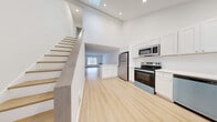 Located at Putnam Green in Greenwich, CT, this two-story, one-bedroom, one-bathroom residence offers a clean, modern aesthetic with light hardwood flooring and a crisp white palette throughout. The main floor is anchored by an open-concept living, dining, and kitchen area that benefits from soaring ceilings and a skylight, creating an airy, sun-filled atmosphere. The kitchen is well-appointed with white shaker cabinetry, stainless steel appliances including a refrigerator, range, microwave, and dishwasher, plus in-unit stacked washer and dryer for added convenience. A staircase with light wood treads leads to the upper level, which houses the generously sized bedroom featuring a double-door closet and additional storage. The full bathroom is finished in a bright, neutral palette with a white vanity, tiled flooring, and a full tub-shower combination. The living area on the main floor is bathed in natural light from a large window with outdoor views, and baseboard heating is present throughout. With three closets total and a dedicated utility room, this residence offers practical storage solutions alongside its refined, modern design.