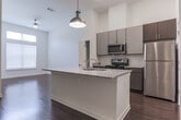 Located on Atlanta Student Movement Boulevard SW in Atlanta, GA, this single-floor residence offers a thoughtfully designed open-concept layout with contemporary finishes throughout. Rich, dark hardwood flooring extends across the main living and kitchen areas, creating a warm and cohesive aesthetic.

The kitchen is a standout feature, equipped with stainless steel appliances including a range, microwave, and refrigerator, complemented by two-tone gray and dark wood cabinetry and a classic white subway tile backsplash. A central island with a granite countertop and undermount sink serves as both a functional workspace and a natural gathering point, accented by a stylish brass pendant light above.

The open living area benefits from soaring ceilings and large windows that invite generous natural light, with a ceiling fan adding comfort to the airy space. The bedroom continues the elevated ceiling height, featuring plush carpeting, expansive windows with blinds, and ample natural light.

The bathroom is clean and well-appointed, showcasing hardwood-style flooring, a granite-topped vanity with dark wood cabinetry, a soaking tub, and white tile surround. A dedicated in-unit laundry closet with a full-size washer and dryer adds everyday convenience. The overall ambiance is modern, bright, and functional.