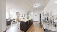 This thoughtfully designed 3-bedroom, 1-bathroom unit offers a functional and modern living experience across a single floor. The open-concept kitchen, dining, and living area serves as the heart of the home, anchored by a large granite-topped island with seating for four — ideal for casual dining or entertaining. The kitchen is outfitted with stainless steel appliances, dark lower cabinetry, crisp white upper cabinets, and granite countertops, combining style with practicality. Hardwood-style flooring runs throughout the main living areas, adding warmth and continuity. The living room receives generous natural light through large windows with outdoor greenery views, creating an inviting, comfortable atmosphere. Each of the three bedrooms is cozy and well-proportioned, with windows that frame pleasant outdoor views and carpeted flooring. The primary bedroom, while compact, is efficient in its use of space. The shared bathroom features dark tile flooring, a granite-topped vanity with dark cabinetry, a full shower/tub combination, and a large mirror. Additional conveniences include dedicated closets, a hallway connecting the private spaces, and an in-unit laundry area, making this a complete and practical living space.
