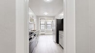 Located at 283 S Center St in Orange, NJ, this single-floor unit offers a thoughtfully updated interior with a clean, modern aesthetic throughout. The galley-style kitchen is a standout feature, outfitted with white shaker cabinetry, granite-look countertops, a stainless steel refrigerator, a gas range, and a classic subway tile backsplash. Light wood-look flooring runs through the kitchen, lending a bright, contemporary feel, while a pair of windows at the far end fills the space with natural light. The living and bedroom areas showcase beautifully refinished hardwood floors with a warm honey tone that contrast elegantly against the soft gray walls and crisp white trim. Crown molding adds a classic architectural detail throughout these rooms, and windows provide ample natural light. The bathroom is finished in all-white vertical tile, featuring a full soaking tub, a vanity with under-cabinet storage, and chrome fixtures, creating a clean and serene atmosphere. The floor plan, visible in the dollhouse view, reveals a well-organized, elongated layout with clearly defined rooms flowing efficiently from one to the next. Overall, the unit presents a polished blend of classic architectural character and modern updates.