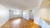 This 2-bedroom, 1-bathroom unit is thoughtfully laid out across a single floor, offering a practical and cohesive living space. Warm parquet hardwood flooring runs throughout the main living areas and bedrooms, adding a classic character to the interior. Crown moulding and textured ceilings are consistent features throughout, contributing to a clean, finished aesthetic.

The open living area is bathed in natural light through a wide window, creating a bright and welcoming atmosphere. A hallway with parquet flooring connects the living area to the rest of the unit, with an adjacent galley-style kitchen featuring light wood cabinetry, white quartz countertops, a stainless steel sink, and tile flooring. A pass-through opening connects the kitchen visually to the living space.

Both bedrooms continue the parquet flooring and offer windows with views of the surrounding urban skyline. The primary bedroom includes a sliding mirrored closet, while the second bedroom also benefits from natural light and direct hallway access. The bathroom is finished with floor-to-ceiling beige tiles, an accent mosaic border, a soaking tub with shower, and a mirrored vanity. A centrally located hallway provides efficient circulation throughout the unit.
