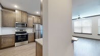 This single-story residence offers a thoughtfully designed layout with contemporary finishes throughout. The kitchen serves as a functional centerpiece, equipped with stainless steel appliances including a refrigerator, range, and microwave. Medium-toned wood cabinetry provides ample storage, while granite-style countertops extend to a peninsula that offers additional workspace and a casual seating area. Light wood-look flooring runs through the kitchen and living areas, lending a cohesive, modern aesthetic.

The living area is generously proportioned, featuring vaulted ceilings accented by crown molding, a ceiling fan with a light fixture, and a row of large windows fitted with blinds that invite natural light. Multiple carpeted bedrooms offer quiet, comfortable retreats, each with windows for natural light. One bedroom includes access to a spacious walk-in closet outfitted with multi-level wire shelving for organized storage.

The unit includes two bathrooms. One features a single-sink vanity with a granite-style countertop and a shower-tub combination, while the second offers a double-sink vanity beneath a large framed mirror, also paired with a shower-tub combo. Light wood-look flooring carries through both bathrooms, maintaining design consistency across the entire residence.