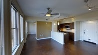 This single-floor residence offers a thoughtfully designed open-concept layout that connects the living, dining, and kitchen areas into one cohesive, flowing space. The polished concrete floors throughout lend an industrial-modern aesthetic while providing durability and a clean, sophisticated look. A ceiling fan anchors the main living area, adding both function and a subtle design touch, while a second ceiling fan is visible in the adjacent room, ensuring comfortable airflow throughout.

The kitchen is a standout feature, boasting dark-stained cabinetry with sleek hardware, stainless steel appliances including a built-in microwave and range, and a peninsula-style island with a sink that serves as both a workspace and a natural divider between the kitchen and living areas. Pendant lighting hangs above the peninsula, complementing the track lighting that illuminates the kitchen and adds a warm, layered glow to the space.

An accent wall in a warm golden-tan hue provides a visual focal point and adds depth to the otherwise neutral color palette of soft whites and beiges. Large windows along one wall invite natural light to pour in, enhancing the open and airy ambiance. The overall design balances contemporary style with practical functionality, creating a welcoming and versatile living environment.