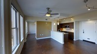 This single-floor residence offers a thoughtfully designed open-concept layout that connects the living, dining, and kitchen areas into one cohesive, flowing space. The polished concrete floors throughout lend an industrial-modern aesthetic while providing durability and a clean, sophisticated look. A ceiling fan anchors the main living area, adding both function and a subtle design touch, while a second ceiling fan is visible in the adjacent room, ensuring comfortable airflow throughout.

The kitchen is a standout feature, boasting dark-stained cabinetry with sleek hardware, stainless steel appliances including a built-in microwave and range, and a peninsula-style island with a sink that serves as both a workspace and a natural divider between the kitchen and living areas. Pendant lighting hangs above the peninsula, complementing the track lighting that illuminates the kitchen and adds a warm, layered glow to the space.

An accent wall in a warm golden-tan hue provides a visual focal point and adds depth to the otherwise neutral color palette of soft whites and beiges. Large windows along one wall invite natural light to pour in, enhancing the open and airy ambiance. The overall design balances contemporary style with practical functionality, creating a welcoming and versatile living environment.