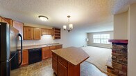 Located at 1261 Tenth Ave NE in Sauk Rapids, Minnesota, this single-floor, one-bedroom, one-bathroom unit offers a well-organized layout across a comfortable footprint. The open-concept kitchen and living area form the heart of the home, with the kitchen featuring warm-toned knotty wood cabinetry, a peninsula island with countertop seating, black appliances including a refrigerator, range, and dishwasher, open shelving with a built-in wine rack, a double stainless steel sink, and durable tile-style flooring. A pendant chandelier adds a decorative touch above the island. The adjoining living room is carpeted and filled with natural light from large windows, with baseboard heating running along the exterior walls. The primary bedroom is a generously sized room with carpet flooring, a window, and baseboard heating. The full bathroom includes a tub-shower combination, a vanity, and a mosaic tile floor. A closet and hallway round out the functional layout. Textured ceilings are consistent throughout the unit, and warm neutral wall tones create a cohesive, understated atmosphere throughout the space.