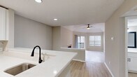 Located at 4901 Tall Timber Dr in Raleigh, NC, this single-floor, three-bedroom, one-bathroom home offers a well-designed layout with modern updates throughout. Light wood-tone flooring runs continuously across the space, complementing the neutral warm-gray walls and white trim found in every room.

The open-concept kitchen and living area serves as the heart of the home. The kitchen features white shaker cabinetry with matte black hardware, white quartz countertops, a marble-style tile backsplash, and a full suite of stainless steel appliances including a refrigerator, range, over-the-range microwave. A peninsula with an undermount sink and matte black faucet opens toward the living area. The living room is highlighted by vaulted ceilings, a ceiling fan, a tile-surround fireplace, and sliding glass doors that lead to a private outdoor deck with wooded views.

The spacious primary bedroom benefits from vaulted ceilings, a ceiling fan, and direct access to a closet. The additional bedrooms are well-proportioned, each with natural light from windows fitted with blinds. The shared bathroom includes a white vanity with quartz countertop, an undermount sink, matte black fixtures, and a framed mirror. A dedicated closet with wire shelving provides additional storage.