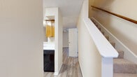 This two-story residence offers a well-organized layout across both levels, unified by light-toned wood-look flooring that flows consistently throughout the main living areas. The entry hallway provides a clear sightline through the home, with a staircase featuring a wooden handrail leading to the upper level.

The living room serves as the central gathering space on the main floor, highlighted by a tile-surround fireplace, a ceiling fan, and track lighting. French doors open to the exterior, allowing natural light to fill the room. An open pass-through connects the living area to the kitchen, which is equipped with warm honey-toned wood cabinetry, white countertops, a stainless steel range, black dishwasher, black microwave, and a double-basin sink.

The bedrooms are generously sized, each featuring wood-look flooring, neutral walls, and large windows fitted with horizontal blinds that provide ample natural light and outdoor views. At least one bedroom includes a sliding-door closet with built-in shelving. The bathroom includes a wood-framed vanity mirror, single-basin sink, white countertop, and matching wood cabinetry, maintaining a consistent warm aesthetic throughout the home.