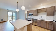This 2-bedroom, 2-bathroom unit in Middleton, WI offers a thoughtfully designed single-floor layout that makes efficient use of its space. The open-concept kitchen and living area serves as the heart of the home, featuring warm hardwood-style flooring, taupe cabinetry with gold hardware, white quartz countertops, and a central island illuminated by modern globe pendant lights. Stainless steel appliances, including a gas range, dishwasher, microwave, and refrigerator, complete the well-equipped kitchen. The living area opens to a private balcony through sliding glass doors, offering natural light and neighborhood views. Both bedrooms are carpeted and feature warm wood-trimmed oak doors, with the secondary bedroom including a ceiling fan and a sizable window. The two bathrooms are finished with wood-toned cabinetry, white countertops, and tile flooring, maintaining a consistent, cohesive aesthetic throughout. A dedicated closet provides additional storage. The unit's clean white walls, warm wood accents, and consistent finishes create a bright, modern ambiance well-suited for comfortable everyday living in the Middleton community.