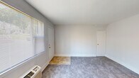 This single-floor unit offers a straightforward and functional layout, thoughtfully organized across several distinct areas. The open living space is finished with neutral gray carpeting and crisp white walls, creating a clean, versatile backdrop. Large windows dressed with horizontal blinds allow generous natural light to fill the room, while a wall-mounted PTAC unit provides individual climate control. A tiled entryway transitions smoothly into the carpeted main area, and multiple doorways provide easy access to the rest of the unit.

The kitchen is efficiently designed, featuring warm honey-toned oak cabinetry above and below the countertops, a stainless steel single-basin sink, light laminate countertops, a dishwasher, and a full-size refrigerator. The tile flooring in the kitchen adds durability and easy maintenance. A pass-through counter opens the kitchen toward the living area, enhancing the sense of connectivity.

Two bedrooms offer comfortable, carpeted spaces, each with windows that bring in natural light and individual wall AC units for personalized temperature control. The bathroom is clean and functional, featuring a single vanity sink with chrome fixtures and a mirrored medicine cabinet above. Throughout the unit, white trim and neutral tones contribute to a bright, cohesive atmosphere.