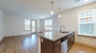 Located at 3750 Philemon Ave in Charlotte's 28205 zip code, this single-floor residence offers a thoughtfully designed open-concept layout that seamlessly connects the kitchen, dining, and living areas. The kitchen is a standout feature, equipped with dark espresso cabinetry, granite countertops, a central island with a built-in sink and dishwasher, and a full suite of stainless steel appliances including a refrigerator, range, and microwave. Pendant lighting above the island adds a polished, modern touch. Light hardwood-style flooring flows throughout the main living areas, complementing the clean white walls and creating a bright, airy atmosphere. The living area benefits from multiple windows dressed with blinds, allowing ample natural light and access to an outdoor balcony. The bedrooms offer plush carpeting, ceiling fans, and generous windows with outdoor views, while the primary bedroom includes a walk-in closet. The bathroom is finished with a granite-topped dark wood vanity, wood-look flooring, and a tiled tub-shower combination with brushed nickel fixtures. Throughout the space, consistent finishes and contemporary design elements contribute to a cohesive, move-in-ready environment.