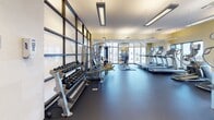 Located at 1910 Towne Centre Blvd in Annapolis, Maryland, this well-appointed fitness center offers a comprehensive workout environment designed to meet a wide range of exercise needs. The single-floor facility is generously proportioned, providing ample space for members to move freely between equipment zones without feeling crowded.

The cardio section is equipped with multiple treadmills and elliptical trainers, all positioned to take advantage of the expansive floor-to-ceiling windows that line the perimeter walls. These large windows flood the space with natural light and offer open views of the surrounding Towne Centre area, creating an energizing atmosphere during workouts.

The strength training area includes a multi-station cable and weight machine system, a dedicated bench press station, and additional cable pull-down units, catering to a full range of resistance training exercises. A well-stocked dumbbell rack with a broad selection of free weights completes the strength equipment offering.

Large mirrors are mounted along key walls, enhancing the sense of space and allowing users to monitor their form throughout their workout. The flooring features a durable dark rubberized surface designed for both safety and performance. Overhead linear lighting supplements the natural light, ensuring the space remains bright and well-illuminated at all times. The overall design is modern, clean, and functional.