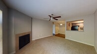 This single-story residence offers a practical and comfortable layout across several well-defined living spaces. The main living area is generously proportioned, anchored by a tile-surround fireplace and topped with a ceiling fan that provides both style and ventilation. Neutral-toned carpet flows throughout the living and bedroom areas, while wood-look flooring defines the kitchen, hallway, and bathrooms, creating a clear distinction between zones.

The kitchen is equipped with black appliances, including a refrigerator and electric range, complemented by light-toned countertops and ample cabinetry. A pass-through opening connects the kitchen to the living area, enhancing the sense of openness. A pendant light fixture adds a subtle design touch above this transition.

A hallway leads to the private quarters, including a bedroom featuring carpet flooring, a window with outdoor greenery views, and direct access to an adjoining room. Two bathrooms are present, each outfitted with a tub-shower combination and wood-look flooring. The neutral gray wall tones and white trim found throughout the space create a clean, cohesive aesthetic that is both functional and inviting.
