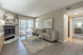 This thoughtfully designed single-story residence offers a cohesive, neutral aesthetic throughout its efficiently arranged floor plan, encompassing a bedroom, living room, dining room, kitchen, laundry room, two closets, and connecting hallways. The living room serves as the heart of the home, anchored by a white-surround fireplace and bathed in natural light from a large sliding glass door that opens to an outdoor view. Light-toned wood-style flooring runs through the main living areas, complementing the warm beige walls and textured ceiling. The adjacent dining area provides an intimate space for meals, featuring light wood-style flooring and a soft, neutral backdrop. The galley-style kitchen is well-equipped with gray shaker cabinetry, light quartz countertops, a textured tile backsplash, stainless steel appliances including a range, microwave, and refrigerator, and a double-basin sink with a modern matte black faucet. Track lighting overhead enhances both function and style. The generously sized bedroom is carpeted for comfort and features a window that fills the room with natural light, along with direct access to a walk-in closet with built-in shelving. A dedicated in-unit laundry room with side-by-side washer and dryer and overhead shelving adds everyday convenience to this well-rounded home.