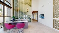 This 180-square-foot stairwell, located at 2157 E Apache Blvd, Suite 360, in Tempe, Arizona, serves as a visually dynamic transitional space within the building. The staircase features warm wood-toned treads that transition in tone from rich, dark walnut at the base to lighter wood finishes toward the upper landing, creating a layered visual effect as one ascends.

The most distinctive design element is the bold, floor-to-ceiling multicolor striped mural that lines the stairwell walls. Composed of vertical bars in an eclectic palette—including red, teal, navy, yellow, green, and neutral tones—the artwork lends the space a contemporary, gallery-like character. Complementing this vibrant wall treatment are sleek, curved yellow-gold handrails mounted on both sides of the staircase, providing both safety and a cohesive design accent that ties into the mural's color palette.

At the upper landing, the space opens into a bright corridor with white tile flooring, recessed ceiling lighting, and a glazed exterior door that admits natural light. The overall ambiance is energetic and modern, transforming a purely functional circulation space into an engaging architectural experience.
