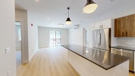 Located at 100 Plank Street in Bedford, MA, this thoughtfully designed 2-bedroom, 2-bathroom residence offers a comfortable and modern living experience across a single floor. The open-concept kitchen and living area serves as the heart of the home, featuring light hardwood flooring, pendant lighting, and a sliding glass door that fills the space with natural light and provides access to a private patio. The kitchen is outfitted with stainless steel appliances, a large island with a dark countertop, a classic white subway tile backsplash, and a combination of white lower cabinets and warm wood-toned upper cabinets for a contemporary aesthetic. The generously sized primary bedroom includes sliding glass door access to the patio and a well-organized walk-in closet system with dual hanging rods and built-in shelving. The second bedroom features dual windows with outdoor views and elegant three-panel interior doors. Both bathrooms are finished with floor-to-ceiling tiled walk-in showers featuring glass enclosures, built-in shelving, and mosaic tile flooring. Additional highlights include five closets for ample storage, a dedicated laundry area, and a connected hallway that ties the layout together efficiently.