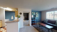 Located at 4300 Collegiate Way in Mount Pleasant, Michigan, this single-floor residence offers a well-organized layout designed for comfortable everyday living. The open-concept living area features bold teal accent walls, soft carpeted flooring, and a large window that allows natural light to fill the space with a bright, welcoming atmosphere. The kitchen is efficiently designed with light wood cabinetry, a white appliance suite including an electric range and refrigerator, a stainless steel sink, and a distinctive red and cream checkered tile floor that adds a retro character to the space. A breakfast bar connects the kitchen to the rest of the living area for easy flow. Adjacent to the kitchen is a dedicated dining area with neutral walls, offering a cozy setting for meals. The two bedrooms are carpeted and well-lit by natural light from ample windows. One bedroom features dark charcoal accent walls, a mirrored sliding closet, and space for a work desk, making it functional as both a sleeping and study area. The second bedroom offers a quieter, lighter palette with neutral walls and a comfortable feel. The full bathroom includes tile flooring, a shower-tub combination, and a vanity with built-in cabinetry, rounding out this practical and characterful home.