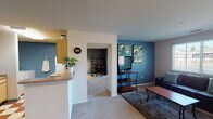 Located at 4300 Collegiate Way in Mount Pleasant, Michigan, this single-floor residence offers a well-organized layout designed for comfortable everyday living. The open-concept living area features bold teal accent walls, soft carpeted flooring, and a large window that allows natural light to fill the space with a bright, welcoming atmosphere. The kitchen is efficiently designed with light wood cabinetry, a white appliance suite including an electric range and refrigerator, a stainless steel sink, and a distinctive red and cream checkered tile floor that adds a retro character to the space. A breakfast bar connects the kitchen to the rest of the living area for easy flow. Adjacent to the kitchen is a dedicated dining area with neutral walls, offering a cozy setting for meals. The two bedrooms are carpeted and well-lit by natural light from ample windows. One bedroom features dark charcoal accent walls, a mirrored sliding closet, and space for a work desk, making it functional as both a sleeping and study area. The second bedroom offers a quieter, lighter palette with neutral walls and a comfortable feel. The full bathroom includes tile flooring, a shower-tub combination, and a vanity with built-in cabinetry, rounding out this practical and characterful home.