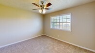 This one-bedroom, one-bathroom unit in Biloxi, Mississippi offers a practical and efficiently organized single-floor layout. The living area features neutral-toned carpet and opens directly to a semi-open kitchen defined by a pass-through counter and warm wood upper cabinetry overhead. The kitchen is equipped with white appliances, including an electric range, refrigerator, and a built-in sink along the counter — all visible from the main living space, creating a connected, functional feel. A textured ceiling runs throughout, consistent with the unit's straightforward design. The bedroom is a well-proportioned carpeted room featuring a ceiling fan with light fixture, a window that brings in natural light with outdoor views, and a sliding-door closet for storage. A secondary door from the bedroom connects to the hallway, improving flow throughout the unit. The bathroom includes a full-size tub and shower combination with white surround panels, a window for ventilation and natural light, and standard fixtures. A hallway connects the main spaces efficiently. Overall, the unit presents a clean, neutral palette with functional features throughout.