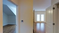 This single-floor residence presents a clean, well-maintained interior designed for comfortable everyday living. The space is characterized by smooth white walls and warm-toned hardwood flooring that flows throughout, lending a sense of cohesion and warmth to the interior.

A central hallway connects the various areas of the home, with a wall-mounted thermostat offering convenient climate control. Louvered closet doors add a classic touch to the layout while providing functional storage solutions. The hallway opens into a bright, airy room anchored by a set of double French doors dressed with white blinds, allowing ample natural light to filter in while maintaining privacy.

The open, uncluttered rooms offer a neutral canvas that can be easily adapted to a variety of furnishing styles and personal preferences. Ceilings are clean and well-proportioned, contributing to the overall sense of space and airiness throughout. A secondary area visible through an adjoining doorway hints at additional rooms, suggesting a versatile and practical floor plan.

Overall, the space presents a bright, move-in-ready interior with consistent finishes, natural light, and functional design elements that make it well-suited for a range of occupants.