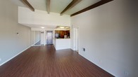 Located at 200 City Blvd W in Orange, California, this single-floor residence offers a thoughtfully designed layout with a distinct architectural character. The living area immediately draws the eye upward to dramatic vaulted ceilings accented by exposed wood beams and a wood-plank ceiling finish, lending warmth and a sense of openness to the space. Rich, dark hardwood-style flooring runs throughout the main living area, complementing the neutral gray walls and clean white trim.

The kitchen is positioned adjacent to the living space and features a breakfast bar pass-through, dark wood cabinetry, granite-style countertops, and black appliances including a refrigerator, range, and built-in microwave. A mosaic tile backsplash adds a decorative touch to this functional cooking area.

The bedroom continues the vaulted beamed ceiling aesthetic and is finished with plush neutral carpeting. A multi-pane window with plantation shutters allows natural light to filter in while offering a view of the surrounding palm-lined exterior. The bathroom includes a vanity with granite-style countertops, white cabinetry, a mirrored medicine cabinet, and wood-style flooring, with an adjacent walk-in closet providing generous storage. The overall ambiance is clean, bright, and comfortable.