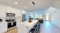 This thoughtfully designed two-story home offers a generous layout across two floors, featuring 2 bedrooms, 3 bathrooms, a dedicated office, and multiple closets for ample storage. The main floor is anchored by a bright, open-concept kitchen, dining, and living area. The kitchen is outfitted with white shaker cabinetry extending to the ceiling, stainless steel appliances, and a large quartz waterfall island with bar seating — all illuminated by sleek pendant lighting and recessed fixtures. The adjoining living area benefits from a wide bank of windows that flood the space with natural light and offer outdoor views, while light-toned hardwood flooring flows seamlessly throughout the main level. A circular pendant light distinguishes the dining area, which comfortably accommodates a round table and chairs. The upper floor houses both bedrooms, each with plush carpeting and generous closet space, including well-shelved walk-in storage. The primary bedroom provides a comfortable, restful retreat. The dedicated office features carpet flooring and a window with exterior views, making it a practical workspace. Three clean, bright bathrooms — featuring white vanities, contemporary fixtures, and hardwood-style flooring — serve the home efficiently. Throughout, the interior maintains a crisp, modern aesthetic with a neutral white and soft grey palette.