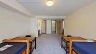 Located at 646 East College Avenue in State College, PA, this 870-square-foot student apartment offers a functional and practical layout across a single floor, comprising six rooms designed to accommodate multiple residents. The unit features multiple carpeted bedrooms, each furnished with lofted twin beds with built-in storage drawers underneath, individual desks, and chairs — providing each resident with a dedicated study and sleep area. Bedrooms are brightened by windows with vertical blinds, allowing natural light to filter in, with views of the surrounding campus neighborhood. A shared full bathroom includes a single-sink vanity with wood cabinetry, a toilet, and a shower/tub combo, finished with tile flooring and a large mirror. The kitchen is equipped with wood cabinetry, granite-style countertops, a black electric range, a microwave, and hardwood-style flooring, offering ample prep and storage space. A central common area connects the rooms and provides space for group dining or studying, with a table and chairs visible from multiple rooms. Additional storage is available through a spacious walk-in closet with wire shelving. Drop ceilings with flush-mount lighting are consistent throughout the unit, maintaining a clean and uniform aesthetic suited for student living.