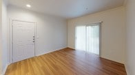 This single-floor residence offers a thoughtfully designed layout with a bright, open feel throughout. The living area makes a strong first impression with warm hardwood-style flooring, crown molding, and a sliding glass door fitted with vertical blinds that fills the space with natural light and provides access to the outdoors. The kitchen is well-equipped with crisp white cabinetry, light countertops, stainless steel appliances including a refrigerator and dishwasher, recessed lighting, and matching hardwood-style flooring that ties seamlessly into the main living area. The bedroom is a comfortable retreat featuring plush carpeting, a large window with horizontal blinds that invites natural light, and a ceiling fan with an integrated light fixture for year-round comfort. Ample storage is provided through a spacious closet outfitted with wire shelving systems, offering practical organization on multiple levels. The full bathroom is finished in a clean, all-white palette, complete with a shower/tub combination, a single-sink vanity with under-cabinet storage, a large mirror, and a stylish multi-bulb light fixture. Overall, the space presents a clean, neutral aesthetic with functional finishes throughout.