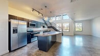 This two-story residence blends modern industrial design with functional living across two well-appointed floors. The main level makes a strong first impression with its open-concept layout, featuring polished concrete floors that extend throughout the kitchen and living areas. The kitchen is a standout, showcasing dark navy cabinetry, stainless steel appliances, granite countertops, and a curved island with pendant globe lighting overhead. Track lighting and a dramatic open staircase with metal railings add to the contemporary aesthetic, while oversized windows flood the space with natural light and offer views of the surrounding area. A spacious living area flows seamlessly from the kitchen, completing the expansive lower floor.

Upstairs, the generously sized primary bedroom features plush carpeting, a ceiling fan, and ample room to accommodate a full suite of furnishings. A walk-in closet with built-in wire shelving provides organized storage. The upper level also includes a second well-proportioned bedroom, also carpeted with a ceiling fan. Three bathrooms serve the home, including one featuring both a separate glass-enclosed shower and a soaking tub with subway tile surround, alongside slate-style tile flooring and dark cabinetry for storage. The thoughtful layout and quality finishes throughout make this a well-equipped and visually striking residence.