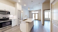 This well-appointed 2-bedroom, 2-bathroom residence in Georgetown, Texas offers a thoughtfully designed single-level layout with modern finishes throughout. The open-concept kitchen and living area serves as the heart of the home, featuring a large center island with a quartz countertop, a gold-toned faucet, and a deep undermount sink. White shaker-style cabinetry reaches toward the ceiling, providing ample storage, while stainless steel appliances — including a French door refrigerator, electric range, and built-in microwave — complete the space. Stylish pendant lighting and recessed fixtures illuminate the area. The living room flows seamlessly from the kitchen, highlighted by a ceiling fan, wood-look plank flooring, and French doors topped with transom windows that open to a private balcony, inviting natural light throughout. Both bedrooms are generously sized with ceiling fans, large windows, and wood-look flooring. The primary bedroom includes a dedicated walk-in closet with built-in shelving and hanging rods. The primary bathroom features a dual-sink vanity with white cabinetry, quartz countertops, and dual mirrors. A second full bathroom and an additional closet with utility hookups round out this clean, contemporary residence.