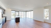 This contemporary single-floor residence showcases a thoughtfully designed open-concept layout filled with abundant natural light. The expansive living area is anchored by large floor-to-ceiling corner windows that frame sweeping panoramic views of the surrounding cityscape, marina, and rolling hills beyond, creating a bright and airy atmosphere throughout. Warm wood-look flooring flows seamlessly across all living spaces, complementing the clean white walls and recessed lighting overhead.

The sleek, modern kitchen is a standout feature, equipped with stainless steel appliances including a gas range, microwave, and dishwasher. Rich dark wood cabinetry reaches to the ceiling for ample storage, while a geometric hexagonal tile backsplash adds a refined design touch. A central island with a white quartz countertop provides additional workspace and casual dining space.

The bedroom offers a peaceful retreat with a large window overlooking lush treetops and a well-proportioned closet with a built-in rod and shelf. The bathroom is finished with large-format tiled walls surrounding a soaking tub and shower combination, a dark wood vanity with a white countertop, and a full-width mirror. A dedicated storage nook adds practical functionality to this polished, move-in-ready space.