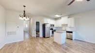 This two-story home presents a clean, modern aesthetic throughout, beginning with an open-concept kitchen and living area on the main floor. The kitchen is well-appointed with white shaker-style cabinetry extending to the ceiling, granite countertops, a central island, and a full suite of stainless steel appliances including a refrigerator, range, microwave, and dishwasher. Light wood-look flooring runs throughout the main living areas, complemented by neutral white walls and recessed and pendant lighting fixtures. A long hallway connects the main living area to the attached garage, with a staircase leading to the upper floor.

The bedrooms are carpeted and bright, each featuring windows with blinds that allow natural light and outdoor views. Closets are outfitted with built-in shelving and hanging rods, offering practical storage. The bathrooms maintain the home's consistent palette with white cabinetry, granite vanity tops, and wood-look tile flooring. One bathroom features subway-tiled shower walls with a soaking tub and brushed nickel fixtures. The attached garage includes an automatic opener and an electrical panel, adding functional utility to the property.