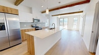 Located at 2500 Bobby Foster Rd SE in Albuquerque, New Mexico, this single-floor unit offers a well-designed open-concept layout that seamlessly connects the kitchen, dining, and living areas. The interior is defined by striking exposed wood ceiling beams that add warmth and character against the clean white walls and ceilings. Light-toned hardwood flooring runs throughout, enhancing the bright, airy atmosphere created by generous natural light.

The kitchen is a standout feature, outfitted with a large waterfall-edge island with an undermount sink, a mix of white upper cabinets and natural wood lower cabinetry, a subway tile backsplash, and a full suite of stainless steel appliances including a french door refrigerator, electric range with microwave, and ample pantry-style cabinetry. Pendant lighting above the island adds a contemporary touch.

The living area opens directly to a private balcony through sliding glass doors, offering views of the surrounding Albuquerque neighborhood. Bedrooms are bright and well-proportioned, benefiting from large windows that invite natural light. Storage is well-addressed with a dedicated walk-in closet featuring built-in shelving and hanging rods. The bathroom includes a full tub-shower combination with clean, white finishes throughout.
