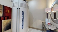 This single-floor tanning studio is designed with functionality and client comfort in mind. The centerpiece of the space is a Sundaze 548V stand-up tanning unit — a professional-grade, full-body tanning system housed in a sleek, upright enclosure with a clean white finish. The room features neutral-toned walls and light tile flooring, creating a bright and hygienic atmosphere that complements the professional equipment. The layout makes efficient use of the available space, allowing easy access to and around the tanning unit. A small side surface, likely used for personal belongings or tanning accessories, is visible alongside the unit, adding a practical touch to the room's setup. Subtle, ambient lighting contributes to a calm and welcoming environment. The overall design is straightforward and purposeful, prioritizing ease of use and a clean aesthetic. Whether used as part of a larger wellness or beauty facility or as a standalone tanning studio, this space provides everything needed for a focused and comfortable tanning experience.