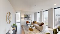 Located in the heart of downtown Columbus on East Broad Street, this sophisticated one-bedroom, one-bathroom residence offers a refined urban living experience with thoughtfully designed interiors and stunning city views throughout. The open-concept living and kitchen area is anchored by expansive floor-to-ceiling windows that flood the space with natural light and frame striking panoramic views of the Columbus skyline. Light hardwood flooring runs through the living and kitchen areas, adding warmth to the contemporary aesthetic. The kitchen is a standout, featuring dark cabinetry with gold hardware, a large white quartz island with seating for three, stainless steel appliances, a white tile backsplash, and stylish pendant lighting. The living room is bright and welcoming, benefiting from corner window exposure that maximizes the city views. The generously sized primary bedroom continues the floor-to-ceiling window theme, offering additional skyline views, soft carpeting, and a ceiling fan. The bathroom is elegantly appointed with large-format tile flooring, a dual-sink dark vanity with gold hardware, white countertops, and an illuminated mirror. A dedicated closet completes the layout, providing practical storage in this well-appointed downtown residence.