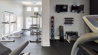 Located at 811 Mallet Hill Rd in Columbia, South Carolina, this single-floor fitness center is a comprehensively outfitted facility designed to support a full range of workout routines. The space is characterized by soaring ceilings adorned with elegant crown molding, light gray walls, and dark rubber flooring — a combination that creates a clean, functional, and motivating environment.

Natural light flows generously through multiple large windows, including clerestory windows positioned high along the walls, enhancing the open and airy feel of the space. White-trimmed French doors and paneled entry doors add a classic architectural touch throughout.

The cardio section features multiple treadmills and additional aerobic equipment, all positioned for comfortable use with wall-mounted flat-screen televisions nearby for entertainment during workouts. The strength training area is well-stocked with a cable machine, a multi-function weight station, a dumbbell rack with a full range of free weights, and adjustable benches. A medicine ball rack and wall-mounted foam rollers round out the functional training offerings.

Large mirrors line portions of the walls, amplifying the sense of space and allowing users to monitor their form. Overhead fluorescent lighting supplements the natural light, ensuring the facility is well-illuminated at all times. This fitness center offers a thorough and accessible workout experience in a polished, well-maintained setting.