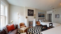 Located at 43 W Long St in the heart of downtown Columbus, Ohio, this single-floor studio unit blends historic architectural charm with thoughtfully modern updates. The open-plan living area serves as the centerpiece of the space, anchored by a decorative brick fireplace with a classic white mantel that adds warmth and character. A bold black-and-white chevron area rug defines the living and sleeping zones, while warm-toned hardwood flooring runs throughout and ties the space together cohesively.

Large double-hung windows flood the interior with natural light and frame views of the surrounding urban streetscape. The living area features a tufted leather sofa and accent seating, creating a comfortable and stylish lounge space. A rustic sliding barn door separates the kitchen area, which is well-equipped with stainless steel appliances, white shaker-style cabinetry, and clean white countertops — offering both functionality and a contemporary aesthetic.

The bathroom is finished with modern grey cabinetry, a white quartz vanity countertop, and light-toned flooring, providing a clean and refreshed feel. Throughout the studio, a mix of industrial, rustic, and classic design elements come together to create an eclectic yet cohesive urban living environment ideal for city living in Columbus.