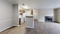 Located at 1207 Kelston Pl in Charlotte, NC, this single-story, one-bedroom, one-bathroom home offers a well-planned layout with distinct functional zones. The open living room serves as the heart of the home, featuring rich dark hardwood-style flooring, a textured ceiling, and a tiled fireplace with a classic white mantle. A sliding glass door floods the room with natural light and provides outdoor access. The kitchen flows seamlessly from the living area and is equipped with warm wood cabinetry, white appliances including a range and refrigerator, and a peninsula with a light countertop that provides additional prep space and separates the two areas. A hallway with a closet connects the main living spaces to the private bedroom. The bedroom is generously proportioned, carpeted for comfort, and benefits from multiple windows that invite ample natural light. A dedicated closet adds practical storage. The full bathroom features wood-look tile flooring, a single vanity with warm wood cabinetry, and a full tub-shower combination with clean white tile surround. Neutral, warm-toned walls throughout create a cohesive and welcoming atmosphere across the entire home.