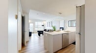 Located at Ferry Wharf in Kelowna, BC, this well-appointed 2-bedroom, 2-bathroom residence offers a clean, modern aesthetic throughout. The open-concept living and kitchen area is anchored by light hardwood flooring and neutral tones that create a bright, welcoming atmosphere. The kitchen is outfitted with sleek flat-panel cabinetry, stainless steel appliances, a white quartz waterfall island with bar seating, and pendant lighting — ideal for both everyday living and entertaining. The living room features large windows framing sweeping views of Okanagan Lake and the surrounding hillsides, with access to a generous balcony that extends the living space outdoors. The primary bedroom is a comfortable retreat with a window showcasing lake and mountain views, while the second bedroom includes a dedicated closet and ample space. Both bedrooms are served by well-designed bathrooms: one features marble-look tile throughout with a glass-enclosed walk-in shower, while the other includes a full soaker tub. Each room benefits from the unit's crisp white walls, recessed lighting, and consistent use of quality finishes. The spacious balcony provides panoramic views of the lake, making it a standout feature of this contemporary Kelowna residence.