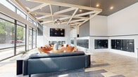 Located at 1003 16th Ave S in Nashville's vibrant Belmont-Hillsboro neighborhood, this amenity space showcases a thoughtfully designed interior spread across a single, generously sized floor. The space is divided into two distinct areas: a sophisticated lobby lounge and a state-of-the-art fitness center.

The lobby lounge makes an immediate impression with soaring ceilings adorned by a striking geometric wood beam framework. Floor-to-ceiling windows flood the space with natural light while offering views of the surrounding streetscape. A large stone-clad fireplace anchors the room, topped with a wall-mounted flat-screen display. Seating is arranged in multiple conversation groupings featuring leather sofas, velvet accent chairs in warm terracotta tones, and a stylish ottoman. Mixed-material tile flooring in coordinating wood and dark tones adds visual depth. A built-in mailbox bank and a secondary lounge nook provide functional touches alongside the elegant entry vestibule with pendant lighting and vertical slat wall detailing.

The fitness center is equally impressive, featuring an extensive array of cardio equipment—including treadmills, ellipticals, and rowing machines—positioned along expansive windows with neighborhood views. A dedicated strength training zone offers cable machines, free weights, and plyometric equipment. A bold perforated ceiling installation with integrated lighting and large wall mirrors complete this high-performance workout environment.